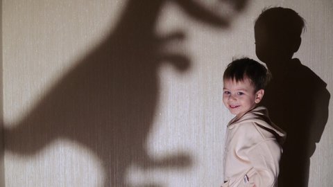 A child plays with a shadow on the wall created by a paper dinosaur