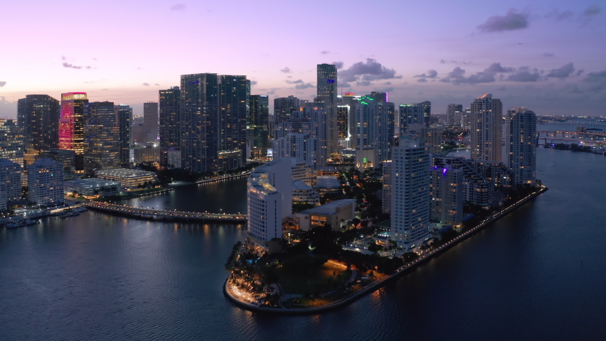 Modern architecture waterfront skyscraper glass buildings in foreground, Miami city in background. USA Florida sunset dusk purple colors of sky. Establishing aerial view shot of Miami downtown skyline