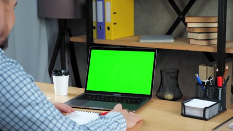Green screen mock up chroma key display monitor laptop computer concept: Laughing businessman at home office sitting on chair at desk tells gesture hand, online business video call webcam meeting chat