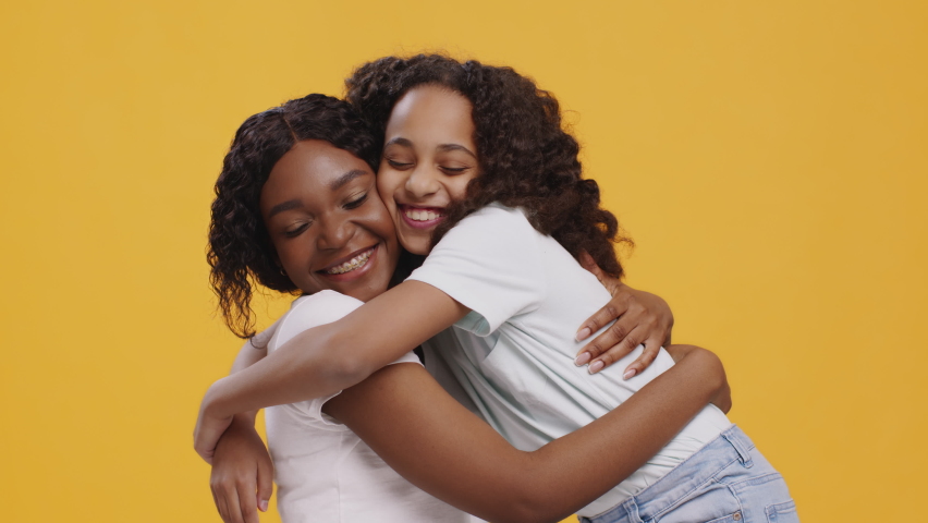 Happy african american girl and woman embracing together, enjoying hugs of each other, orange studio background | Shutterstock HD Video #1068067016