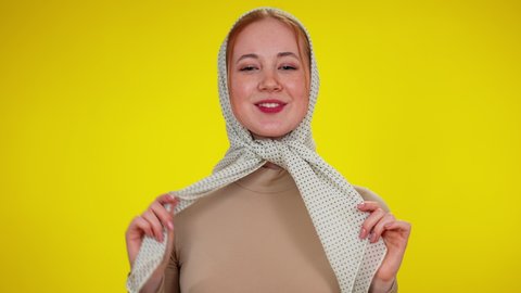 Portrait of young slim redhead woman in kerchief posing at yellow background. Smiling beautiful Caucasian lady looking at camera smiling. Shyness and lifestyle.
