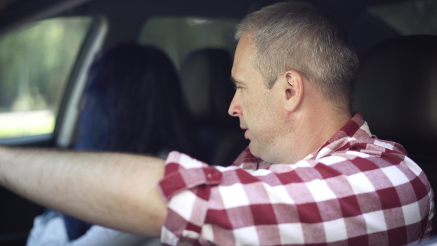 Side view close-up of man talking with blurred stressed woman on passenger seat in car. Adult Caucasian husband arguing with wife in automobile sitting on driver