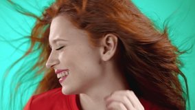 Close portrait of red haired woman smiling and dancing on studio background. Girl in orange bright wear. Positive mood. Slow motion.