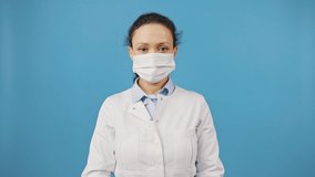 End of epidemic. Cheerful woman doctor taking off protective medical mask, making deep breath and smiling to camera, blue studio background