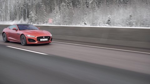 Moscow, Russia - CIRCA 2021: red Jaguar F-type R Coupe driving fast on the highway. Winter forest. Frontview.