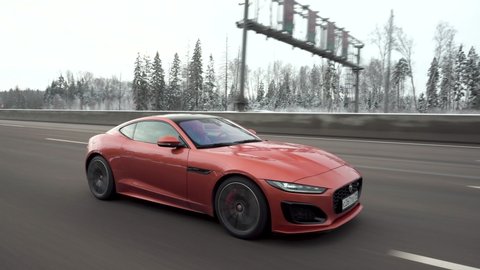 Moscow, Russia - CIRCA 2021: red Jaguar F-type R Coupe driving fast on the highway. Closeup view of spinning wheel