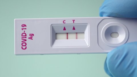 Macro shot of a doctor's hand showing a covid-19 antigen pcr express test cassette with a positive result.