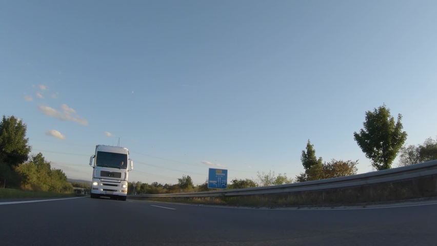 Cargo truck with cargo trailer driving on a highway. White Truck delivers goods in early hours of the Morning - very low angle drive thru close up shot. Royalty-Free Stock Footage #1068073859