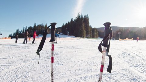 Bukovel, Ukraine - January 12, 2020: Two black ski sticks standing in snow at skiing slope. Plenty of skiers and snowboarders enjoying riding together on snowy mountain. Ski resort. Bukovel, Ukraine.Yaremche