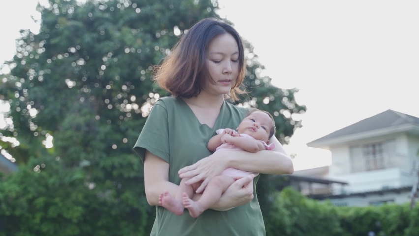 asian woman mother holding sleepy baby infant in garden at luxury home. female parent lull baby by singing a song. natural authentic. Royalty-Free Stock Footage #1068083720