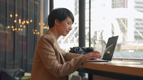 Asian Short hair Businesswoman working with laptop at coffee shop. Confident freelance Asian female short hair working outdoor at coffee shop, Typing on laptop during smile happily.