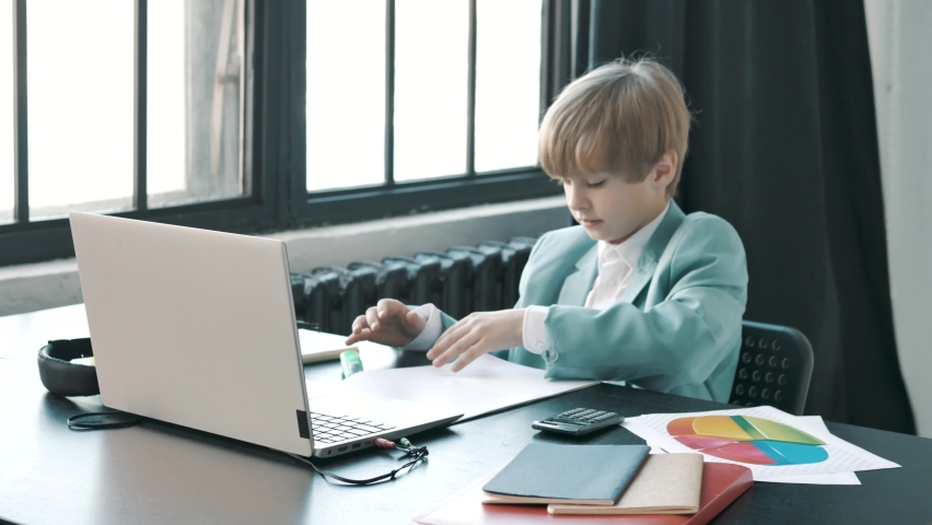 Fucused small child businessman browsing office papers, looking at documents and diagrams, working in modern bright office with laptop. Perspective future for children in business or freelance.  | Shutterstock HD Video #1068087827