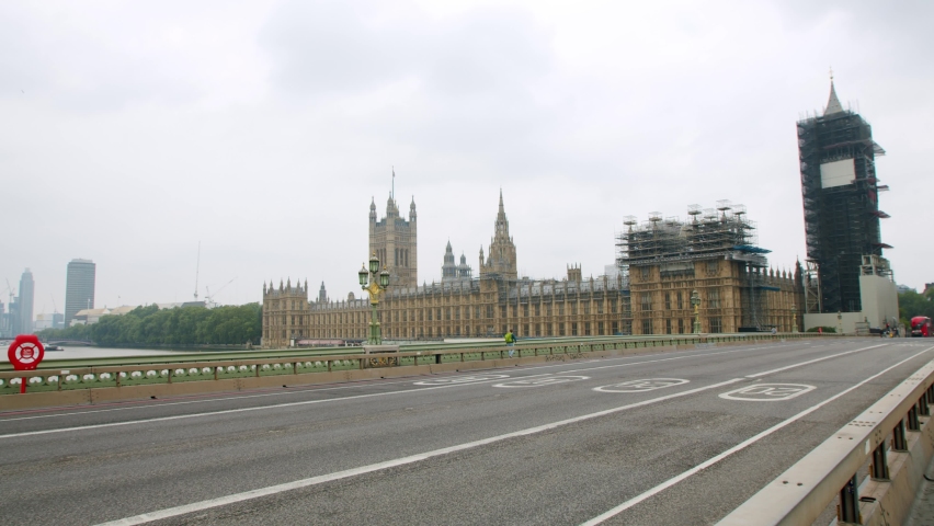 Lone person walks across empty Westminster Bridge, London in front of Big Ben and The Houses of Parliament, during the COVID-19 lockdown pandemic 2020. | Shutterstock HD Video #1068088175