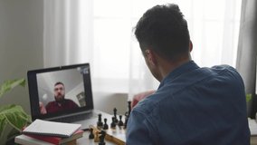 A young cute man gets a lesson on playing chess on a video call at home during a corona pandemic