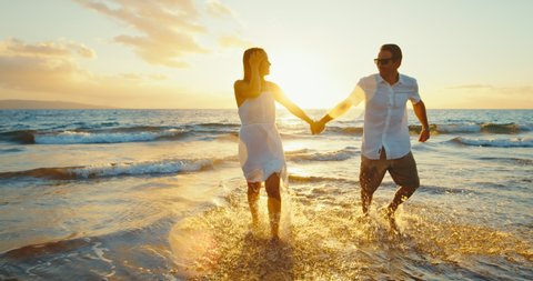 Happy couple in love, playing on the beach at sunset, running and splashing in the waves, travel vacation lifestyle.
