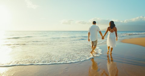Loving couple walking by the shore holding hands at sunset, happy and in love at the beach, paradise and love lifestyle