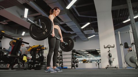 Fit young woman doing deadlift with heavy bar in gym, strong female athlete with muscular body lifting weights, exercising with barbell. Concept of sport, beauty, health, lifestyle. 
