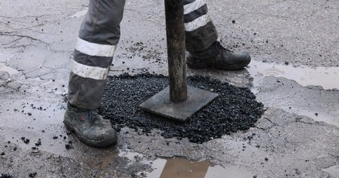 worker pushing bitumen asphalt in the hole. road repair and maintenance