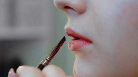 Stylist makes makeup to a woman using a lip brush, beauty, eyeliner. Close-up.