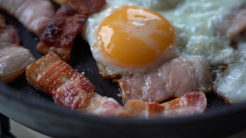 Fried Eggs with Bacon in a Frying Pan. Slices of Toasted Appetizing Bacon and Egg on a Hot Frying Pan. Close-up.