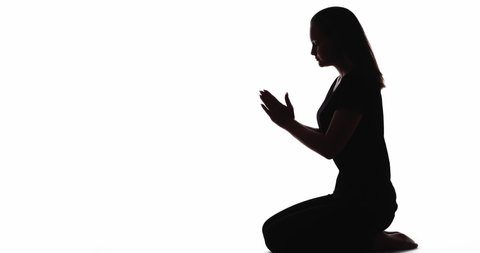 Prayer silhouette. Spiritual belief. Faith hope. Dark contrast profile shadow of peaceful woman kneeling with folded hands isolated on white copy space background.