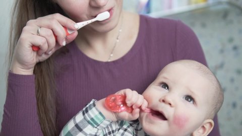 A young mother teaches to brush her teeth with a small child's toothbrush at home in the bathroom.