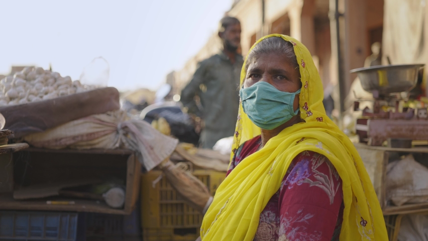Close shot of Indian local market where a traditional female vegetable vendor in colorful attire sitting with a protective mask on face looking at camera during the hard times of covid 19 epidemic | Shutterstock HD Video #1068100184