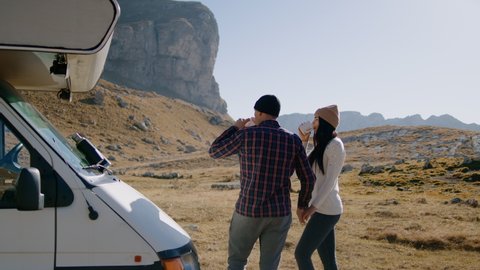 Couple drink coffee by motorhome rv and enjoy picturesque landscape of mountain in autumn. Rbbro man and woman stand by van, hold hands and point hands. Concept look, together, rear view