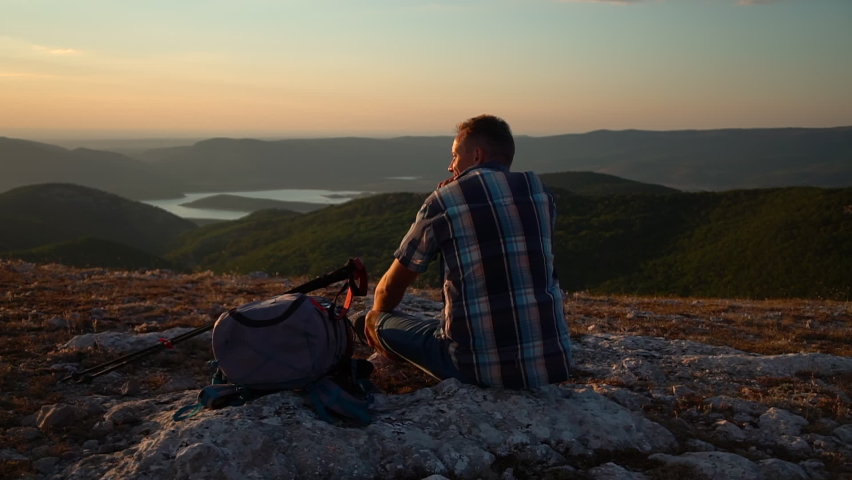adult man rest, sit on mountain hike travel rock and enjoy sunset view. male hiker relax. Spbd meditating tourist backpacker feel freedom and achievement. evening in mountain lake top