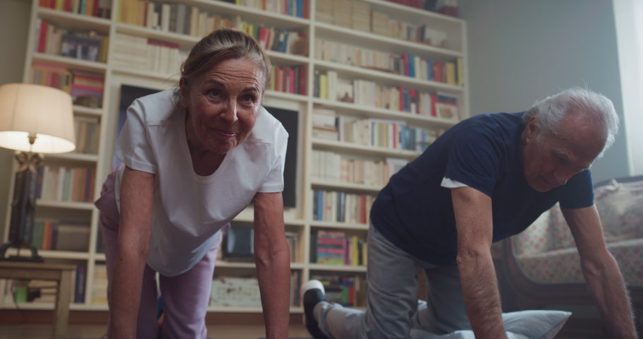 Cinematic shot of happy smiling mature senior couple doing exercises of gymnastics together at home. Concept of healthy lifestyle, fitness, recreation, couple goals, well being, retirement, elderly. | Shutterstock HD Video #1068106478