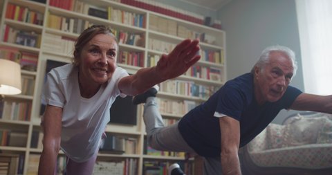 Cinematic shot of happy smiling mature senior couple doing exercises of gymnastics together at home. Concept of healthy lifestyle, fitness, recreation, couple goals, well being, retirement, elderly.