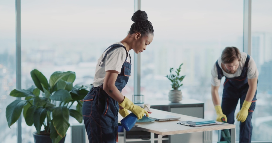 Indoor portrait of afro-americna pretty young woman janitor tidying office room with colleague smiling successful at camera. Cleaning services. Royalty-Free Stock Footage #1068107162