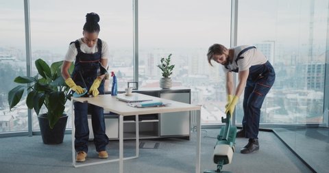 Multi-ethnic team couple of woman and man cleaning corporate office workspace from dirt. Cleaning services people. Vacuum cleaner.