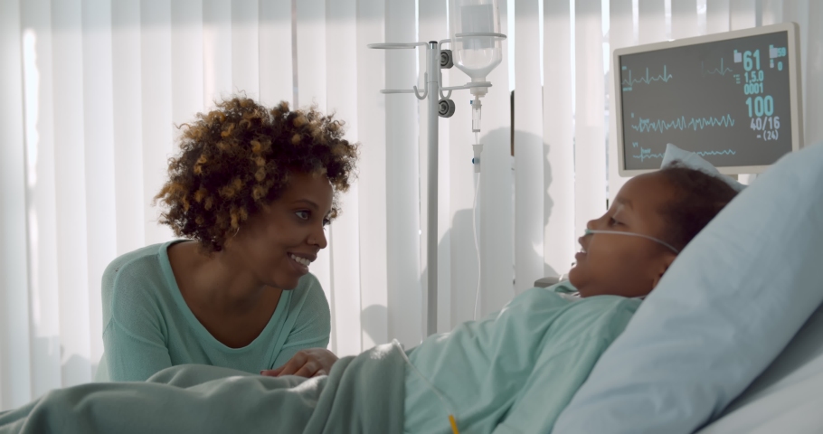 Afro-american mother talking to daughter in intensive care unit. Side view of cute little girl lying in bed and chatting with mother visiting her in hospital ward Royalty-Free Stock Footage #1068116144