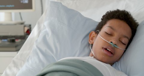 Close up of ill african kid having fever sleeping in bed at hospital. Sick afro-american child lying in hospital bed and sweating suffering from disease