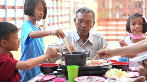 Family grandfather and children eating food party on night of summer holiday, seafood and meat grilling and roasting on pan, happy Asian people family of kids in party, delicious and tasty food menu