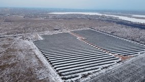 Photovoltaic solar panels standing in snowy field under heavy winter sky near small town. Drone shoots video of energy saving and concept of alternative power source