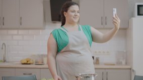 Excited woman in apron filming video about cooking with smartphone, modern job
