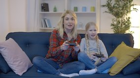 Excited mom and daughter playing video games at home, celebrating victory, fun