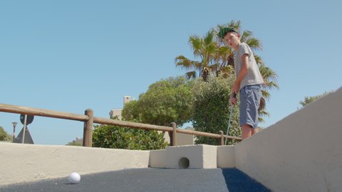 Boy hold golf stick, Hit the mini golf ball and scores a ball into the hole.