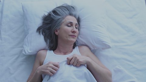 Aged lady with gray hair sleeping in cozy hotel bed, business trip, jet lag