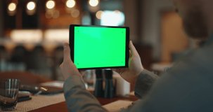 Close up shot of hands of man holding a tablet computer with green chroma key screen. Guy watching a video or having an online chat in cafe - always online 4k template footage