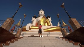 Traveler stands with raised hands up on background Buddhist Thailand temple with big Buddha statue. Beautiful Landmark of Asia. Asian culture, religion and travel destination. 4K