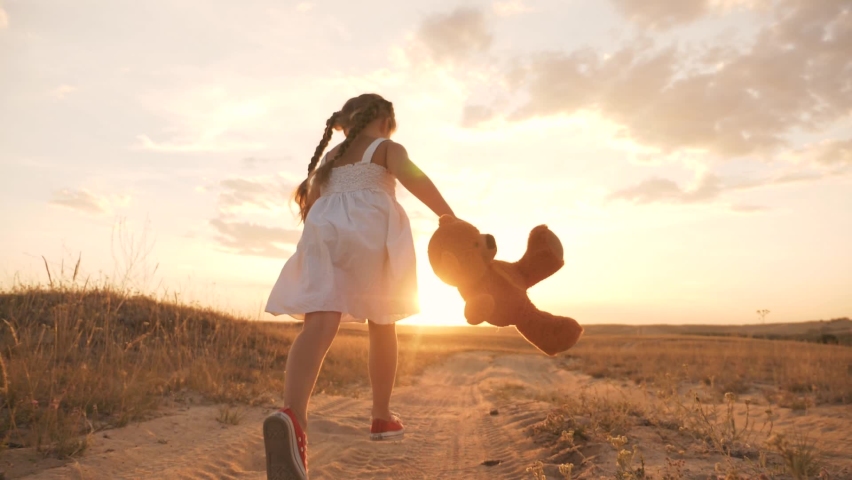 Little girl with a toy teddy bear in park. Cute girl with a teddy bear in a green field. Lonely girl with a toy teddy bear in park in green field.Teddy bear in the hands of a girl in the park Royalty-Free Stock Footage #1068132911