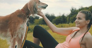 Woman runner and dog on field under golden sunset sky in evening time. Outdoor running. Athletic young female with his dog are running in nature. 4K Video
