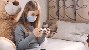 The girl put on masks looks at the phone at home. The COVID-19 pandemic is forcing children to learn online. Kid Using Smartphone Studying Browsing Internet. Home schooling concept for kids.