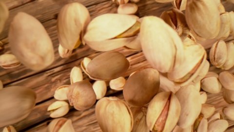Super Slow Motion Shot of Fresh Roasted Pistachio Nuts Falling on Wooden Table at 1000 fps. Top Shot with Camera Motion.