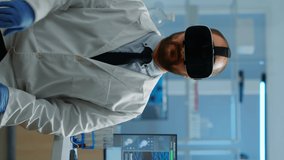 Vertical video: Professional scientist using medical inovation in lab wearing virtual reality glasses, gesticulating. Team of researchers working with equipment device, future, medicine, healthcare
