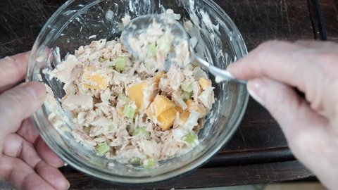 Adding celery, onion mayo and cubed cheese to tuna in a glass bowl making tuna sandwich. Top view
