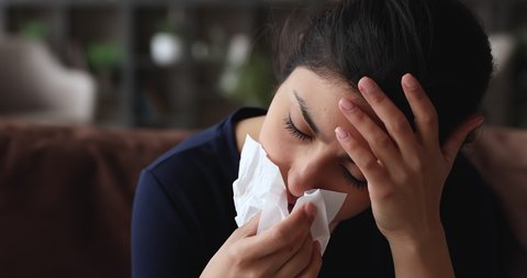 Head shot unhealthy unhappy millennial mixed race indian woman using paper tissue, suffering from runny nose sinusitis nasal infectious disease, feeling uncomfortable at home, first grippe symptoms.